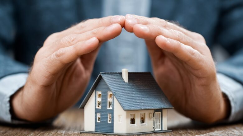 Hands hovering protectively over a miniature house, symbolizing insurance coverage and financial protection
