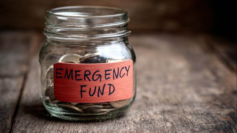 Glass jar labeled “Emergency Fund” partially filled with coins, representing financial preparedness for unexpected expenses