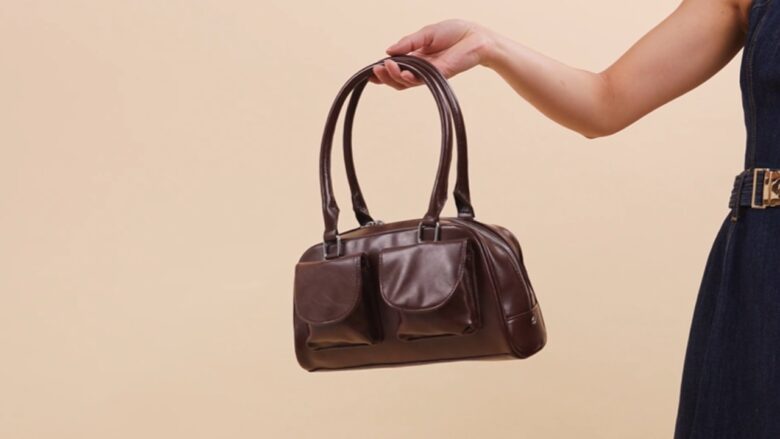 A person holds a brown leather handbag by its handles