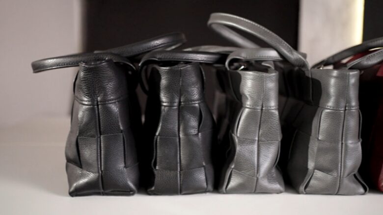 Several black leather bags sit side by side on a shelf