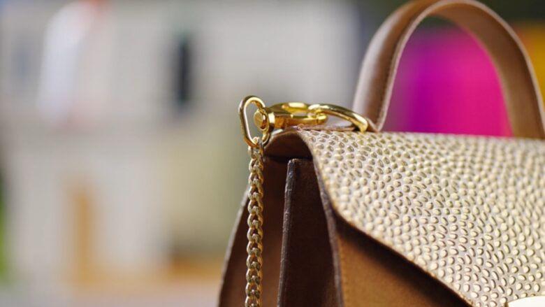 Close-up of a brown leather handbag with gold hardware and a bright pink interior