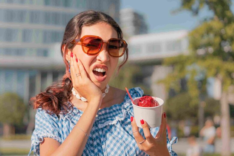 Person holding ice cream and touching their cheek after experiencing tooth sensitivity from a cold dessert