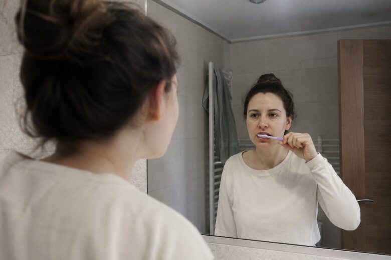 Woman brushing her teeth while looking in the mirror.