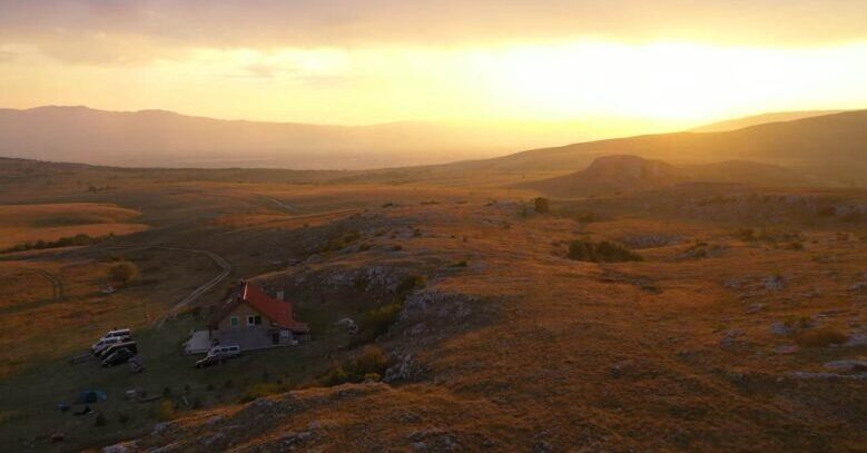 Sunset over the Kruzi plateau near Mount Cincar, showing rolling hills, rocky grasslands and a mountain lodge.