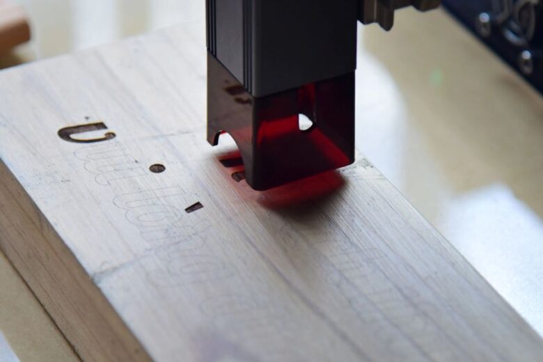 Laser engraving head etching text onto wood, demonstrating detailed marking with a laser cutter.